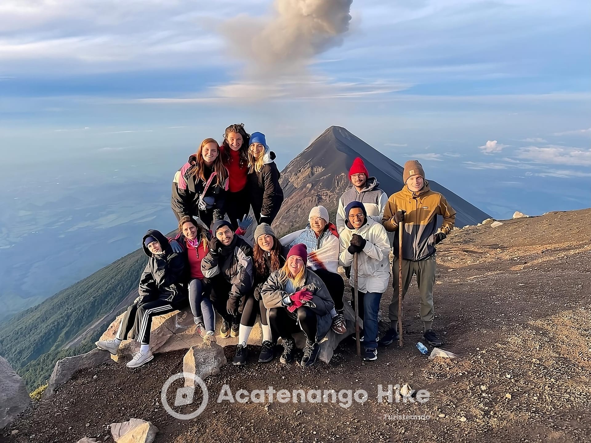 Group photo on the Acatenango summit with smoke rising from Fuego Volcano