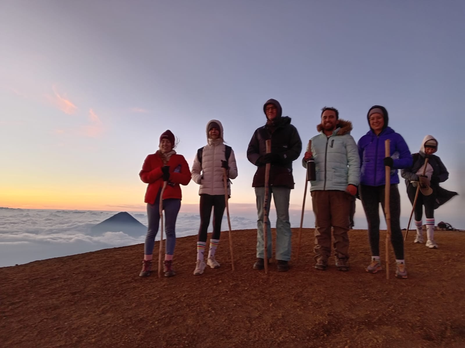 Hikers at the Acatenango summit at sunrise with Agua Volcano above the clouds