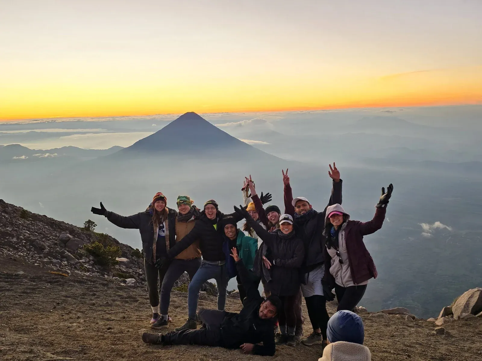Group celebrating at the Acatenango summit at sunrise with Agua Volcano behind